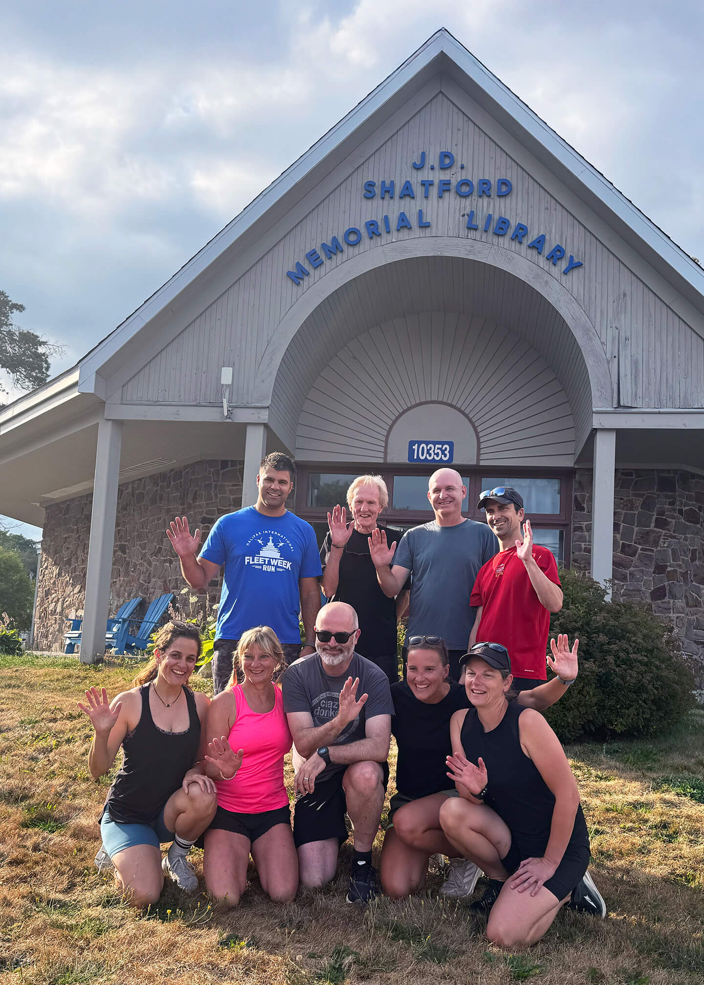 Local Run Club posing outside at the Library entrance, waving and smiling.